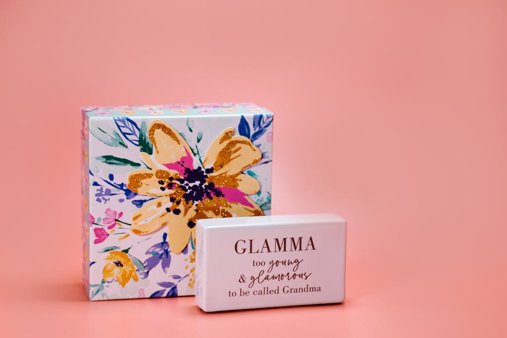 A close-up of a floral gift box and a block with the message 'Glamma' on a peach background, perfect for Mother's Day.